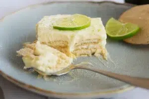 A refreshing slice of Mexican Lime Icebox Cake on a white plate, topped with lime zest and layered cookies, perfect for summer no-bake desserts.