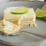 A refreshing slice of Mexican Lime Icebox Cake on a white plate, topped with lime zest and layered cookies, perfect for summer no-bake desserts.