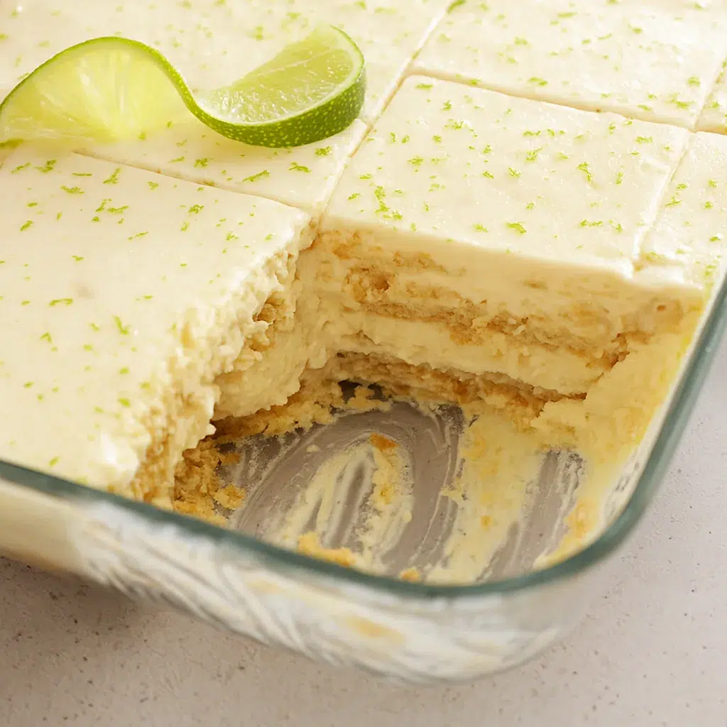 Overhead shot of lime icebox cake topped with whipped cream and a fresh lime slice, set on a white ceramic plate.